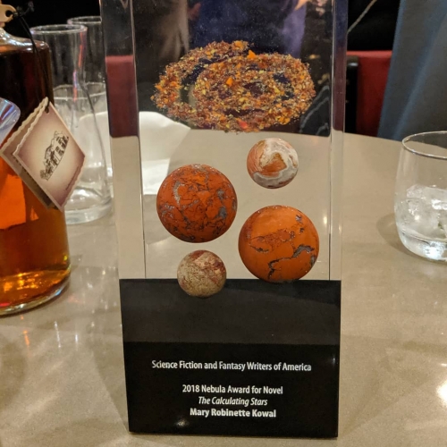 The 2018 Nebula Award for Novel contains reddish stones representing planets and a swirl like a Nebula.