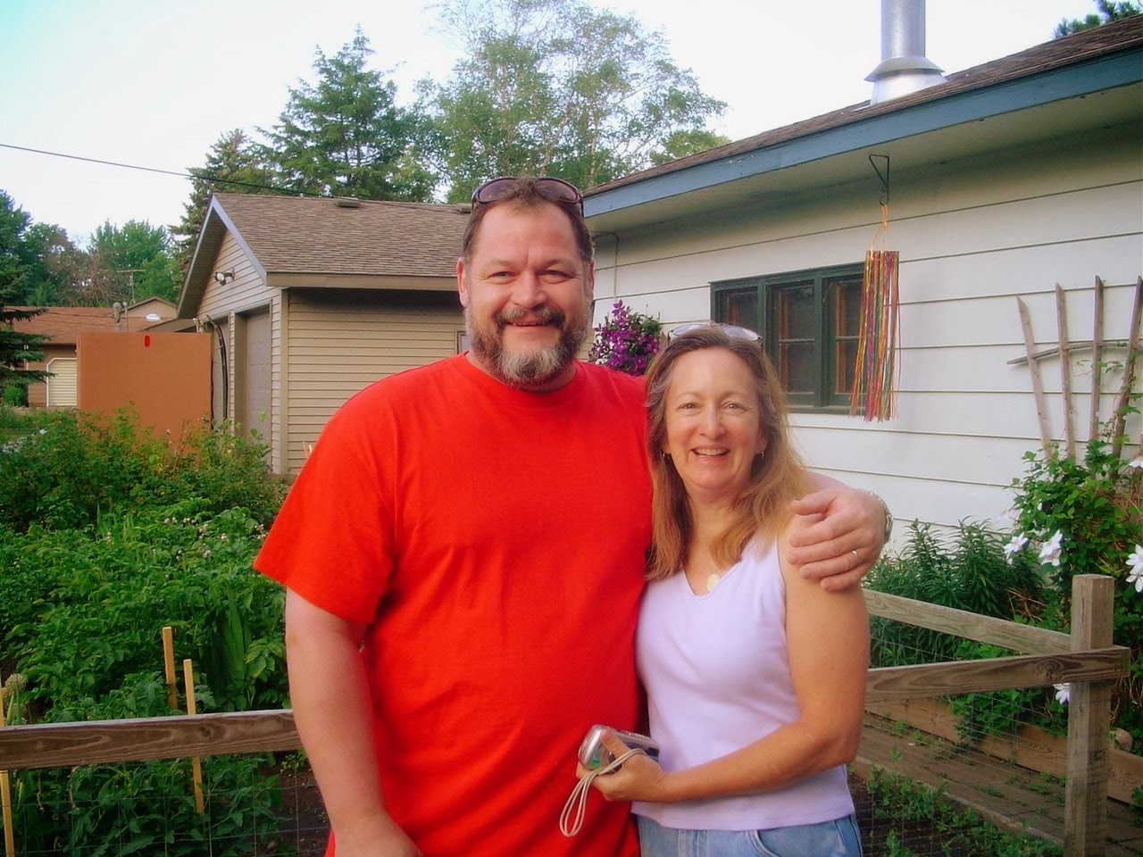 A smiling broadshouldered man and woman in front of a garden