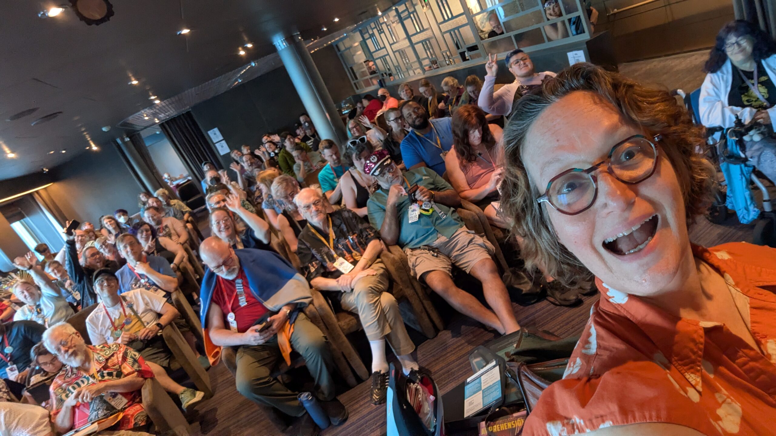 Mary Robinette Kowal standing at the front of a classroom with the audience waving and smiling at the camera.