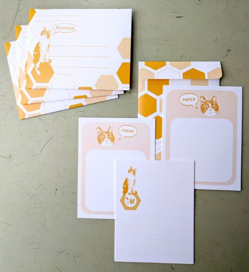 An array of stationary with orange details. A calico cat is on each. Bubbles say "friend" "Delicious" "Hi" and "Paper"